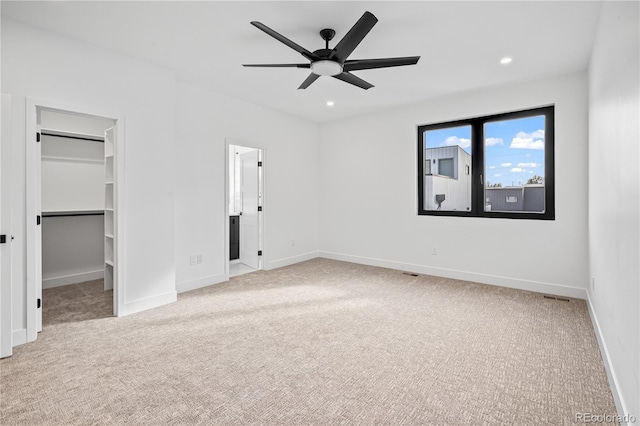 unfurnished bedroom featuring recessed lighting, a walk in closet, light colored carpet, and baseboards