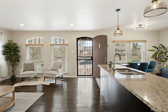 kitchen with pendant lighting, dark wood-type flooring, light stone counters, and a healthy amount of sunlight