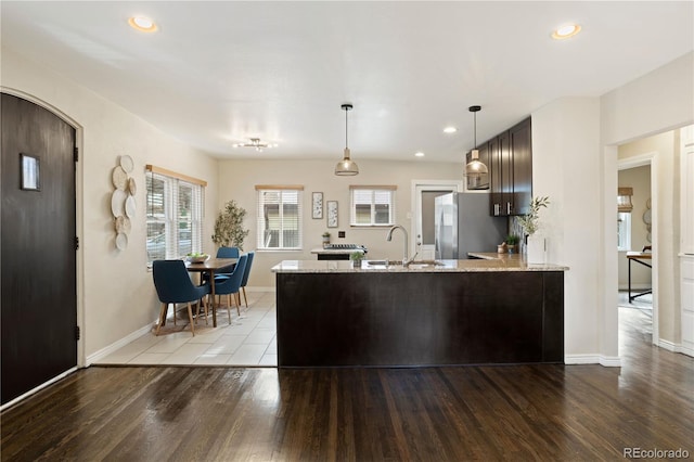 kitchen with sink, stainless steel fridge, light wood-type flooring, light stone counters, and kitchen peninsula