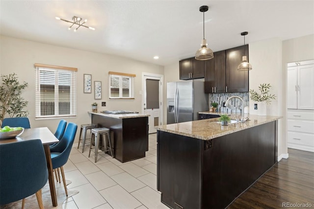 kitchen featuring hanging light fixtures, stainless steel refrigerator with ice dispenser, a kitchen island, dark brown cabinetry, and a breakfast bar area