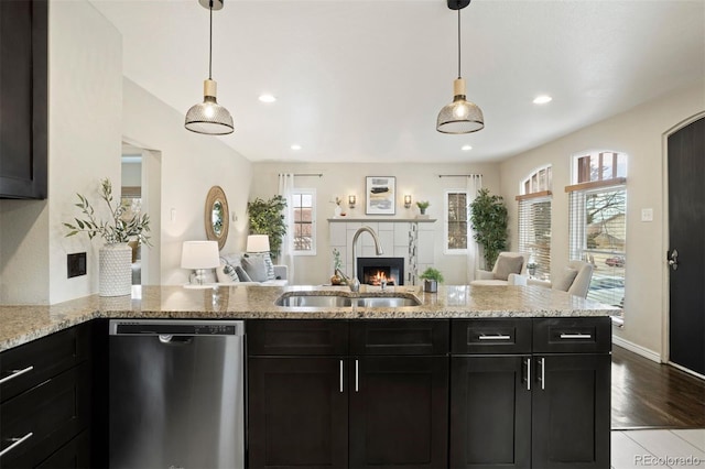 kitchen with dishwasher, sink, light stone countertops, light hardwood / wood-style floors, and a tiled fireplace