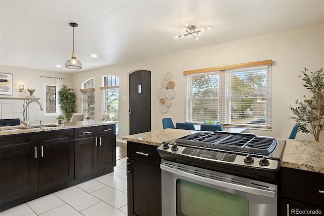 kitchen featuring gas stove, light stone counters, sink, and pendant lighting