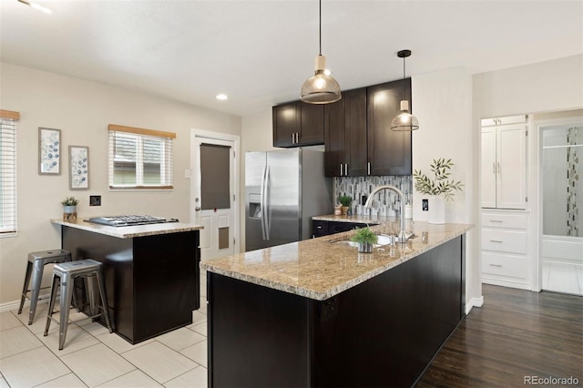 kitchen with stainless steel fridge, dark brown cabinetry, sink, decorative light fixtures, and a kitchen island