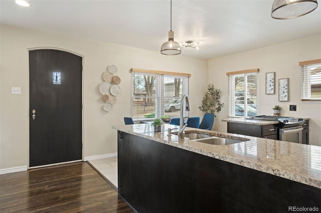 kitchen with pendant lighting, dark wood-type flooring, sink, stainless steel range, and light stone counters