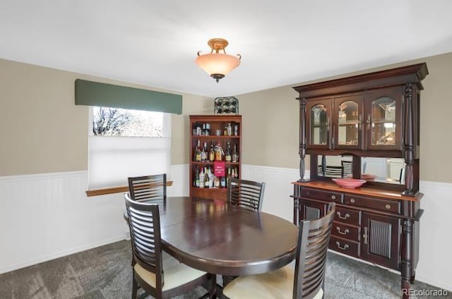 dining area with dark carpet and a wainscoted wall