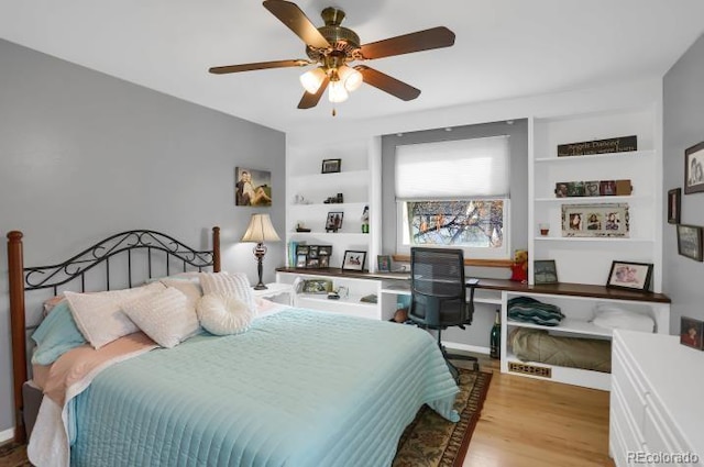 bedroom with built in desk, wood finished floors, and a ceiling fan