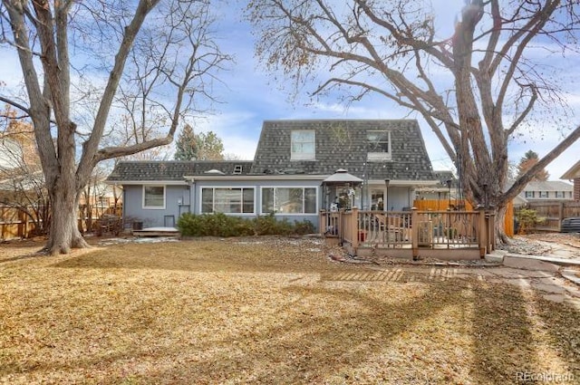 back of house featuring roof with shingles, mansard roof, a wooden deck, and fence