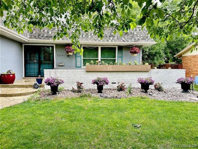 view of front of home featuring roof with shingles, board and batten siding, a front yard, brick siding, and fence