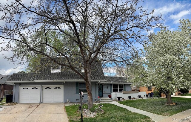 view of front of property featuring roof with shingles, driveway, brick siding, a front yard, and a garage