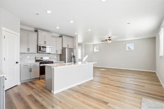 kitchen featuring light countertops, a ceiling fan, a center island with sink, gray cabinets, and stainless steel appliances