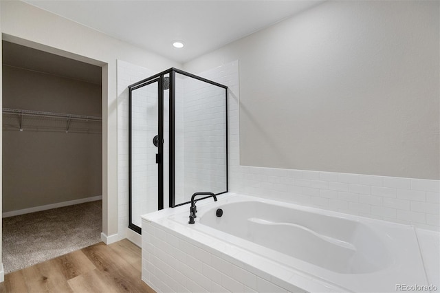 bathroom with baseboards, a spacious closet, a shower stall, wood finished floors, and a garden tub
