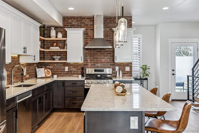 kitchen featuring appliances with stainless steel finishes, a breakfast bar, wall chimney range hood, open shelves, and a sink