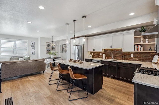 kitchen featuring a sink, light wood-style floors, a kitchen breakfast bar, open shelves, and stainless steel fridge