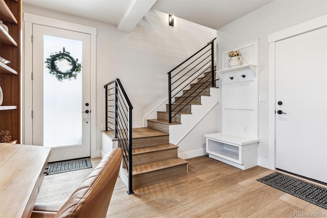 foyer with baseboards, beamed ceiling, light wood finished floors, and stairs