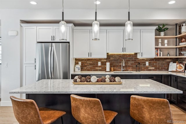 kitchen with light wood-style floors, freestanding refrigerator, white cabinetry, and a sink