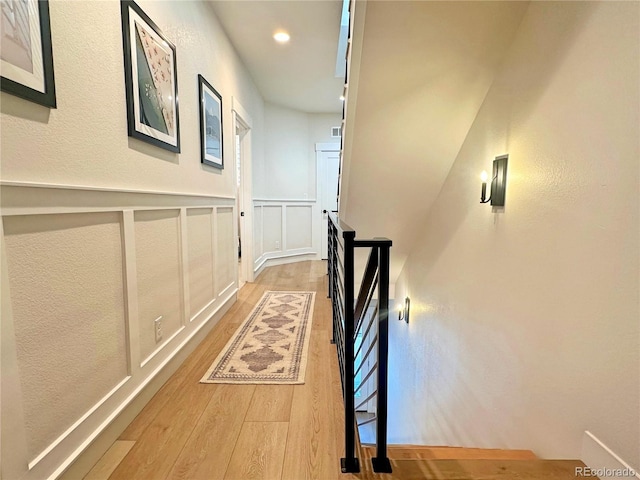 corridor featuring a wainscoted wall, wood finished floors, an upstairs landing, and a decorative wall