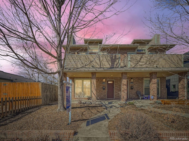 multi unit property featuring a porch, brick siding, fence, and a balcony