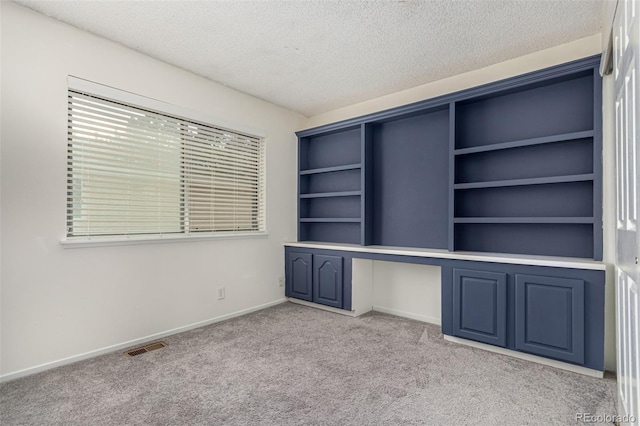 unfurnished office with built in desk, light carpet, and a textured ceiling