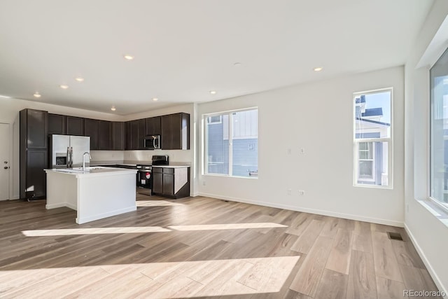 kitchen featuring sink, appliances with stainless steel finishes, dark brown cabinetry, light hardwood / wood-style floors, and a center island with sink