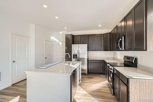 kitchen with sink, light hardwood / wood-style flooring, appliances with stainless steel finishes, a kitchen island with sink, and dark brown cabinets