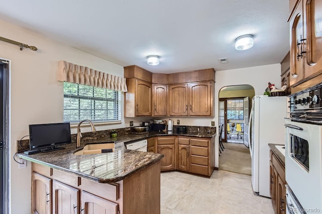 3724 S Poplar St, Denver, CO 80237 - kitchen featuring arched walkways, white appliances, a peninsula, brown cabinets, and dark stone counters