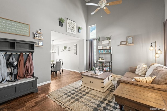 living area featuring ceiling fan, a towering ceiling, wood finished floors, and baseboards