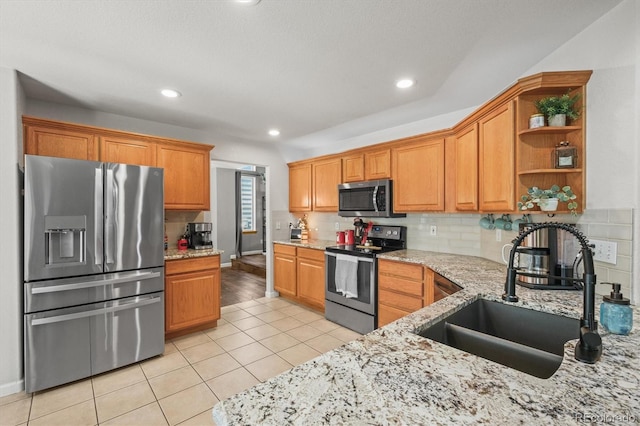 kitchen featuring appliances with stainless steel finishes, a sink, light tile patterned floors, backsplash, and light stone counters