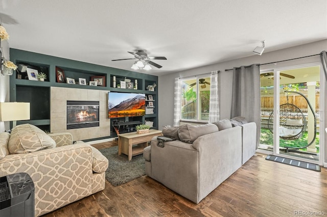 living room with ceiling fan, a tile fireplace, dark wood-style floors, and built in shelves