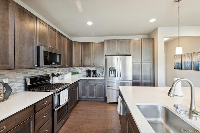 kitchen featuring sink, stainless steel appliances, dark wood-type flooring, tasteful backsplash, and pendant lighting