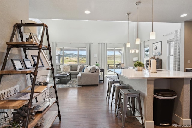 kitchen with a kitchen breakfast bar, a kitchen island with sink, dark wood-type flooring, and hanging light fixtures