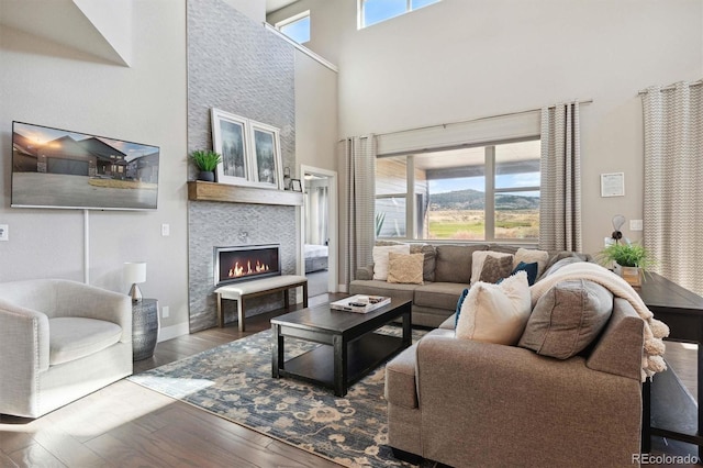 living room featuring wood-type flooring, a fireplace, a wealth of natural light, and a towering ceiling