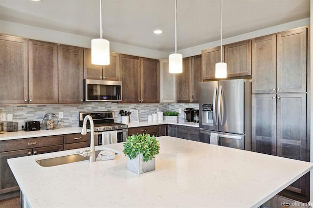 kitchen featuring sink, decorative backsplash, light stone countertops, appliances with stainless steel finishes, and decorative light fixtures