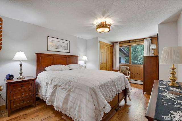 bedroom featuring light hardwood / wood-style floors, baseboard heating, a textured ceiling, and a closet