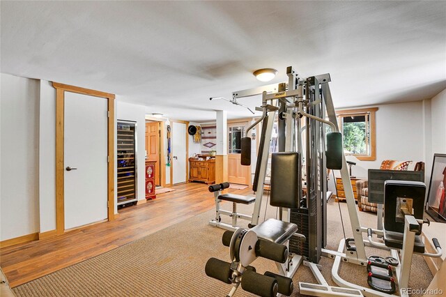 exercise room with light hardwood / wood-style floors and beverage cooler