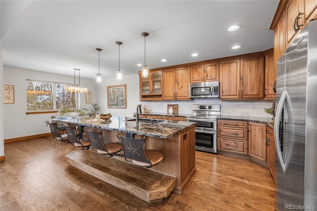 kitchen featuring brown cabinetry, backsplash, stainless steel appliances, a kitchen bar, and a sink