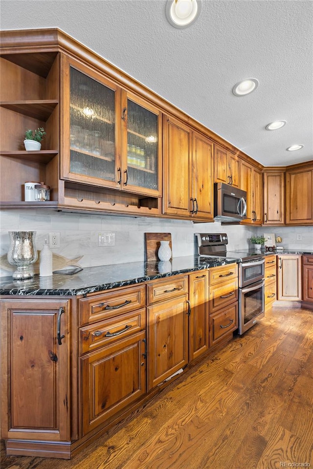 kitchen featuring dark wood-style floors, appliances with stainless steel finishes, brown cabinets, and dark stone countertops