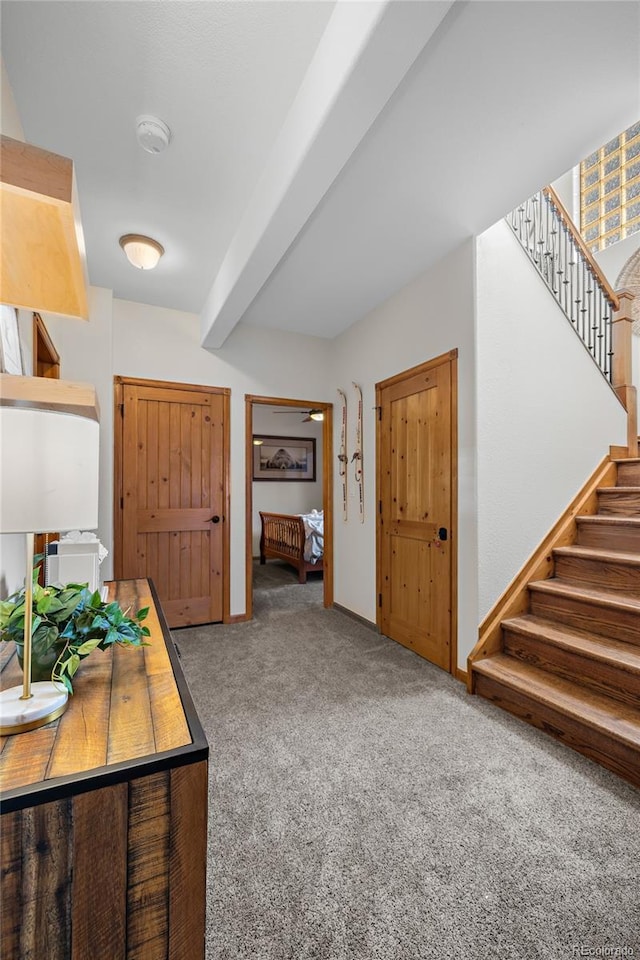 foyer entrance with beamed ceiling, stairway, and carpet flooring