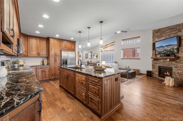 kitchen with open floor plan, a stone fireplace, appliances with stainless steel finishes, and a sink