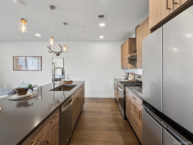 kitchen with dark wood-style flooring, dark countertops, appliances with stainless steel finishes, a sink, and under cabinet range hood