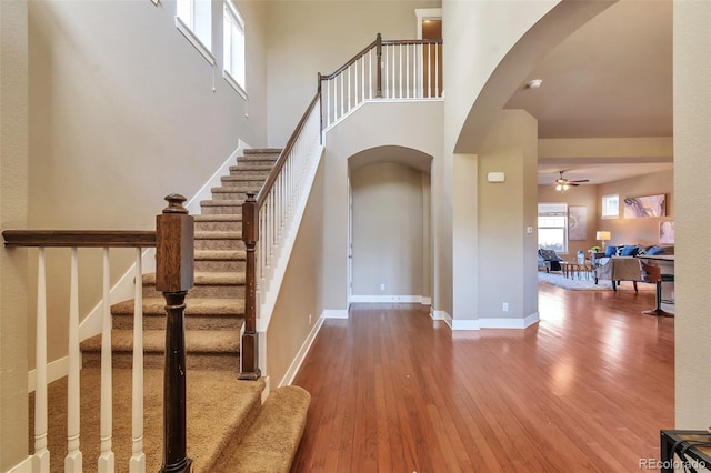 foyer entrance with ceiling fan, wood-type flooring, and a towering ceiling