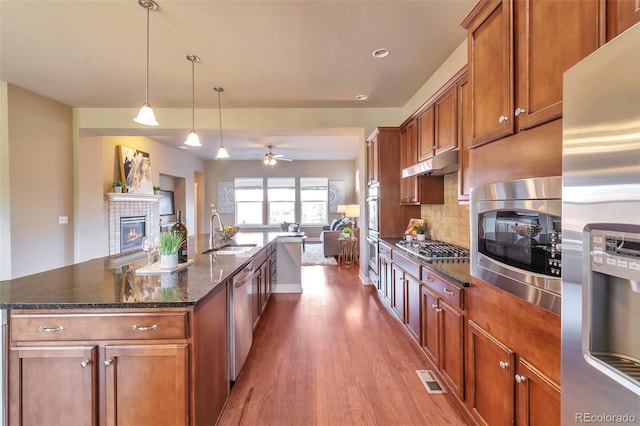 kitchen featuring a tile fireplace, sink, stainless steel appliances, wood-type flooring, and a kitchen island with sink