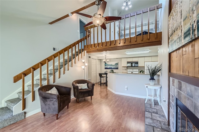 living room featuring a high ceiling, ceiling fan with notable chandelier, hardwood / wood-style flooring, a fireplace, and beam ceiling