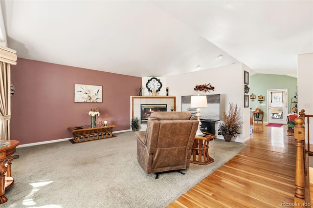 living room with wood-type flooring, a tiled fireplace, and vaulted ceiling