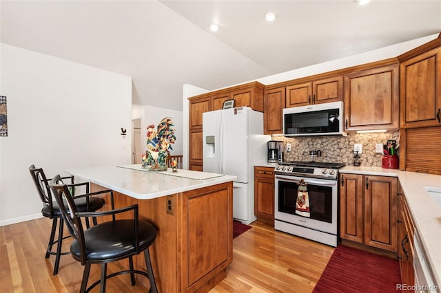 kitchen featuring tasteful backsplash, a breakfast bar area, a center island, white fridge with ice dispenser, and stainless steel gas range oven