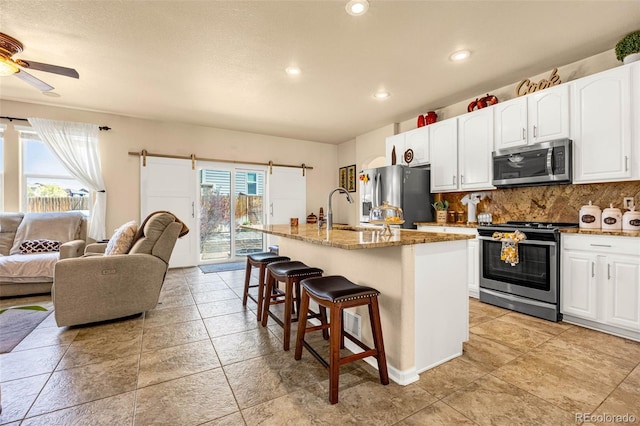 8004 Brittinger Way, Colorado Springs, CO 80951 - kitchen with appliances with stainless steel finishes, open floor plan, a kitchen breakfast bar, a barn door, and stone counters