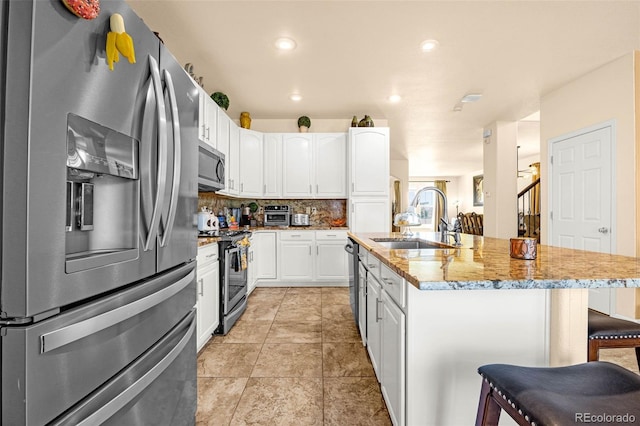 8004 Brittinger Way, Colorado Springs, CO 80951 - kitchen featuring appliances with stainless steel finishes, a kitchen bar, white cabinets, a kitchen island with sink, and light stone countertops