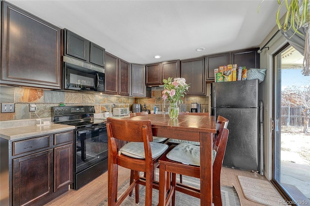 kitchen with light wood-type flooring, dark brown cabinets, backsplash, and black appliances