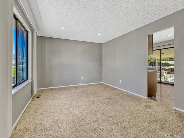 carpeted spare room featuring visible vents, baseboards, a textured ceiling, and recessed lighting