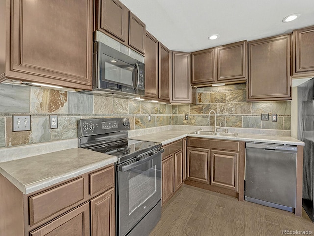 kitchen featuring light wood finished floors, light countertops, a sink, decorative backsplash, and black appliances