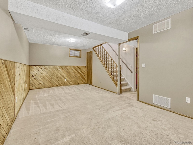 finished below grade area featuring stairway, wood walls, a textured ceiling, and visible vents